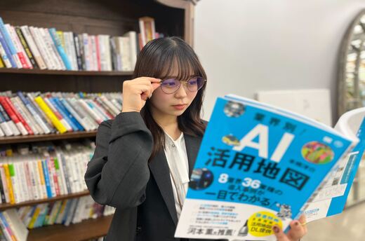 眼鏡をかけ、業界別AI活用地図という本を持っている女性