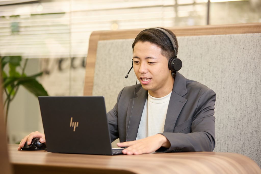 GLOBAL PRODUCE社員がテーブルブースでヘッドフォンをしながらオンラインMTGを受けています。