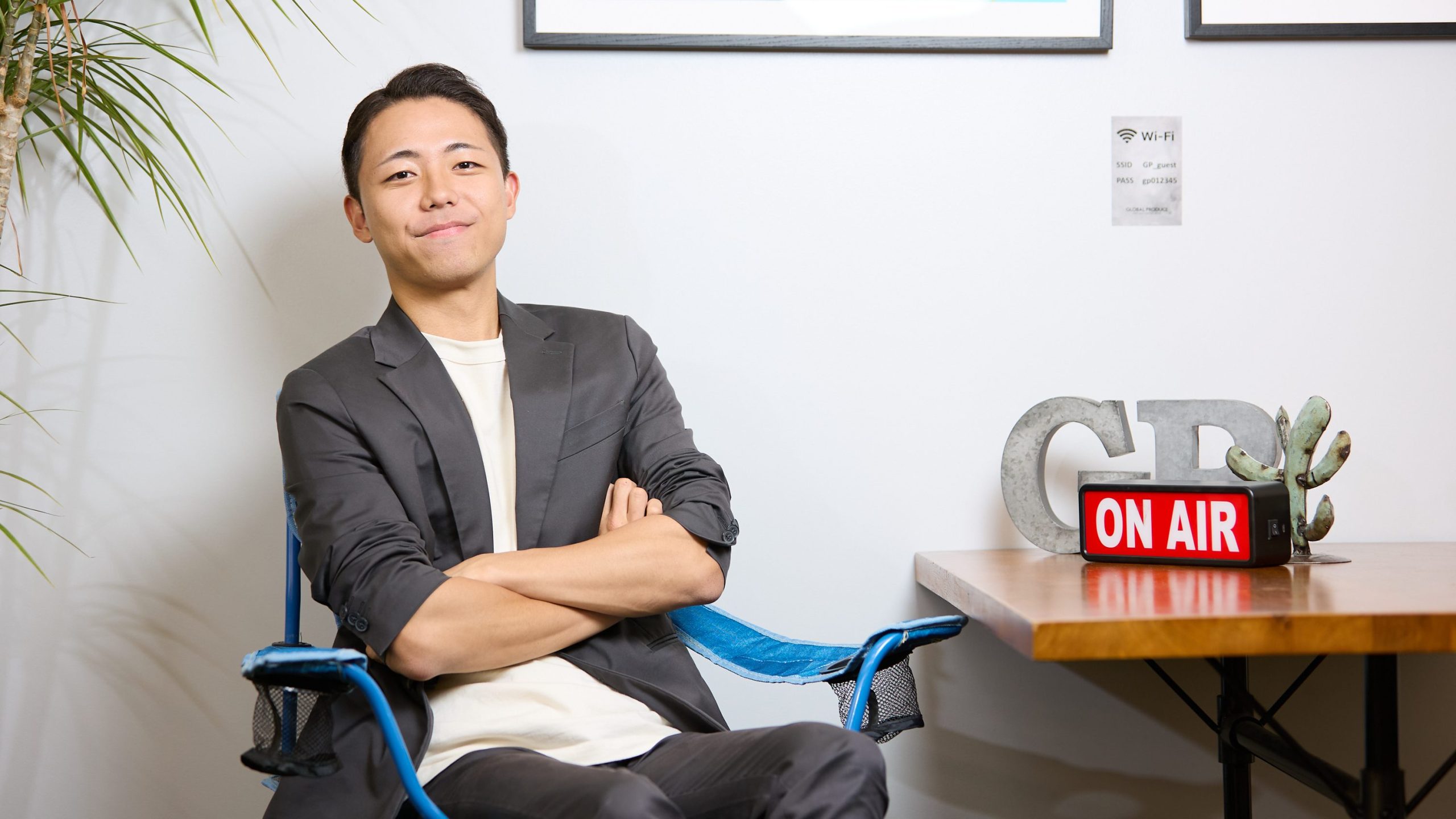 GLOBAL PRODUCEの社員(重田)が壁際のテーブルで、腕を組んでカメラに向かって微笑んでいます。