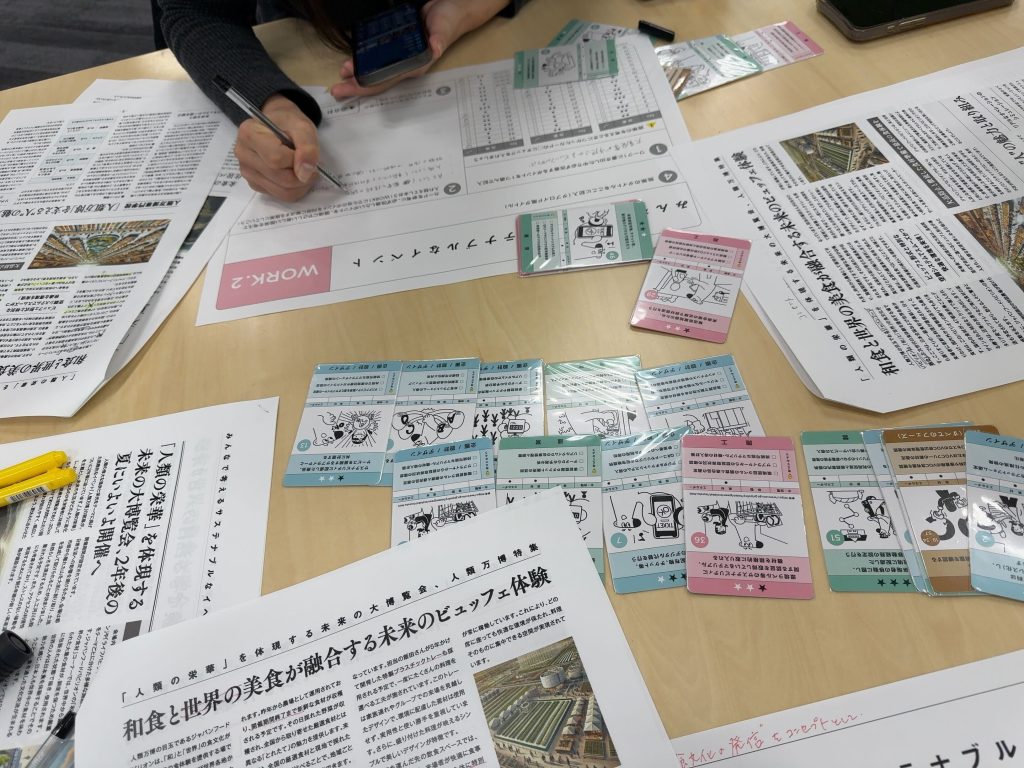 テーブルの上にワークの紙とお題の新聞が置かれ、ワークシートに課題を書いています。