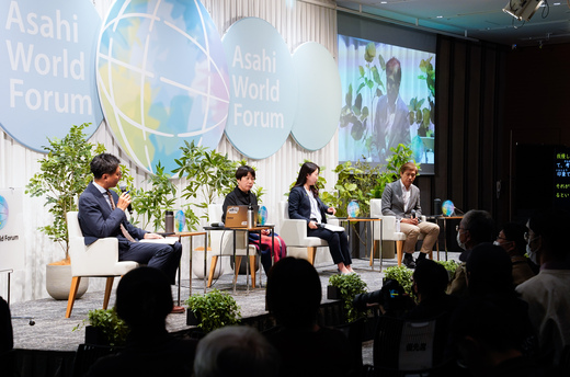 ステージの上で4人がパネルディスカッションを行っている様子。背面には朝日地球会議のロゴである大きな地球のデザインが並び、観葉植物に囲まれたステージを多くの観客が見守っている。