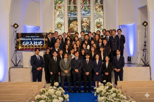 スーツ姿の参加者がステンドグラスの前に並び、入社式で集合写真を撮影している様子。